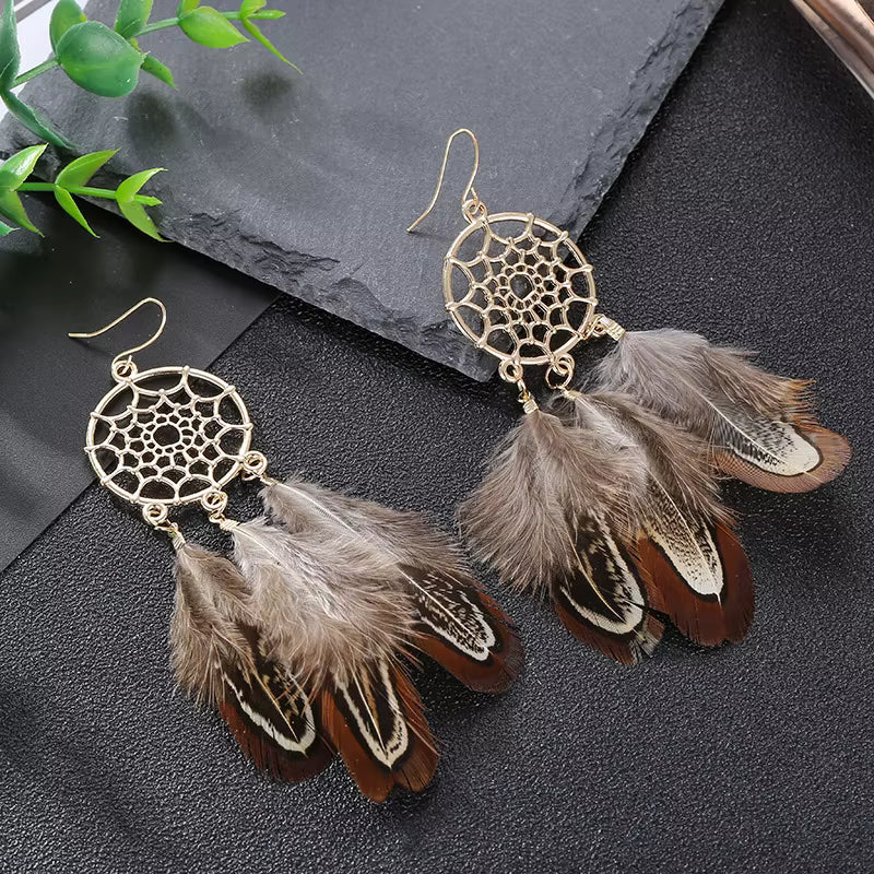 Feathered earrings with gold dreamcatcher design on a dark surface