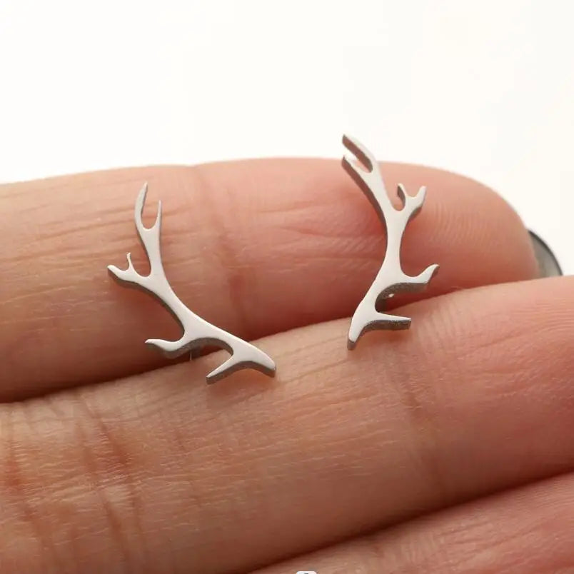 Silver antler-shaped earrings on a hand against a white background