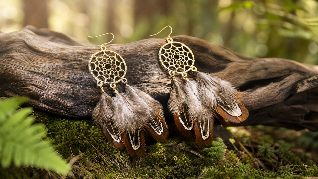 Feathered earrings with gold dreamcatcher design on a log.