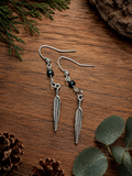 Silver feather drop earrings with iridescent beads on rustic wood with pine cones and eucalyptus