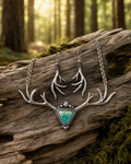 Silver-toned antler necklace and matching drop earrings with a synthetic turquoise triangular stone pendant, displayed on a weathered log in a forest setting.